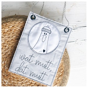 May include: A grey fabric banner with black embroidery of a cartoon bird wearing a hat. The banner has two black eyelets at the top and the text "What mutt, dat mutt" is embroidered in black.