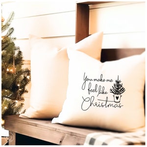 Könnte beinhalten: Ein weißes Kissen mit schwarzem Text, der "You make me feel like Christmas" lautet, mit einem kleinen schwarzen Weihnachtsbaum in einem Eimer mit einem Herzen darauf.