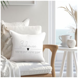 Puede incluir: Almohada blanca con texto negro que dice "Zuhause" con un símbolo de corazón y coordenadas "N 50° 45' 27.07" 0 6° 16' 32.874".