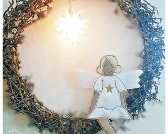 May include: A white felt angel with brown hair and a gold star on its shirt is sitting on a twig wreath. A white star-shaped light is hanging above the angel.