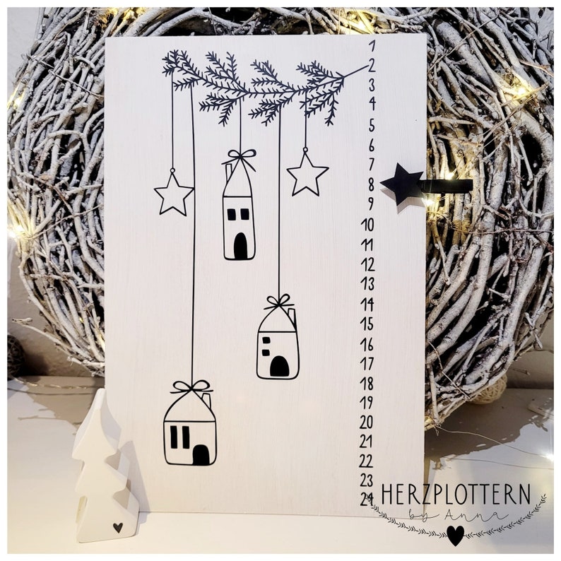 May include: A white wooden advent calendar with black illustrations of houses and stars hanging from a branch. The numbers 1 through 24 are listed on the right side of the calendar. The text "HERZPLOTTERN by Anna" is at the bottom of the calendar.