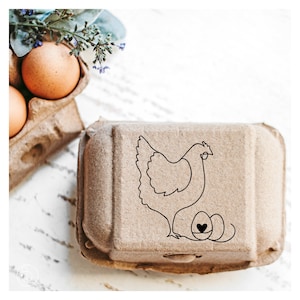 May include: A brown cardboard egg carton with a black line drawing of a hen and two eggs. The hen is facing right and has a heart on one of the eggs.