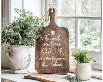 May include: A rustic wooden cutting board with a handle and the text "Freunde sind wie KRÄUTER, sie verfeinern das Leben" in white. The board is displayed with potted herbs and a small wooden cutting board.