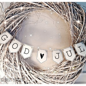 Può includere: Una ghirlanda di rami bianchi con uno striscione che recita "GOD JUL" in lettere nere. Un cuore nero è sullo striscione. La ghirlanda è decorata con piccole luci e brillantini.