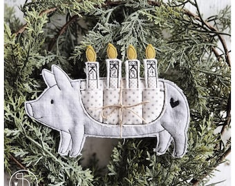 May include: A gray fabric pig ornament with four candles, numbered 1-4, and yellow flames. The pig has a heart detail and is surrounded by a green wreath. The candles are held in a star-patterned holder.