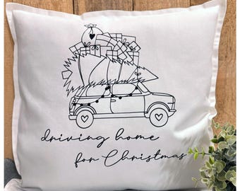 May include: White pillow with a black and white illustration of a car carrying a Christmas tree and presents. The text "driving home for Christmas" is written below the car.