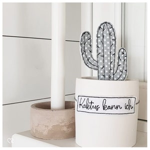 May include: A white ceramic planter with a gray and white polka dot cactus and the text "Kaktus kann ich" in black.