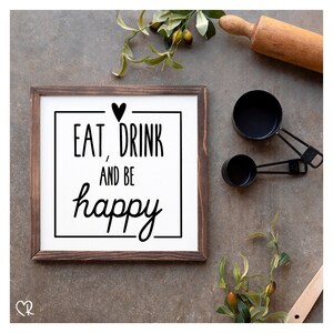 Könnte beinhalten: Ein gerahmtes Schild mit weißem Hintergrund und schwarzem Rahmen. Das Schild sagt "Eat, Drink and be happy" mit einem Herzsymbol über dem Text. Das Schild hängt an einer grauen Wand.