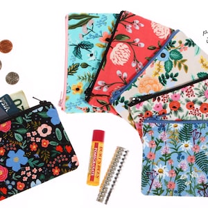 May include: A collection of six rectangular fabric zipper pouches featuring various floral patterns in colors including black, teal, red, cream, and light blue, accompanied by three coins, a credit card, a lip balm, and a metal tube.