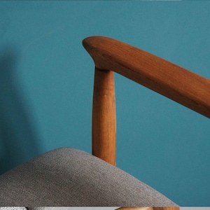 May include: A close-up of a wooden chair armrest with a gray fabric seat. The chair is against a teal blue wall.