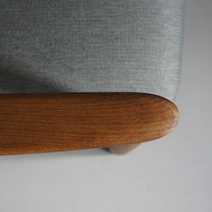 May include: Close-up of a wooden armrest on a light gray fabric chair. The armrest is smooth and has a natural wood grain.