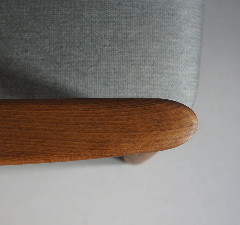 May include: Close-up of a wooden armrest on a light gray fabric chair. The armrest is smooth and has a natural wood grain.