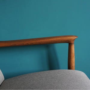 May include: A wooden armchair with a gray fabric seat and a teal blue wall in the background.
