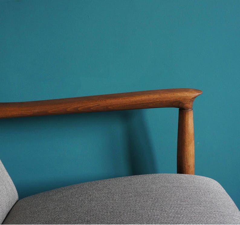 May include: A wooden armchair with a gray fabric seat and a teal blue wall in the background.
