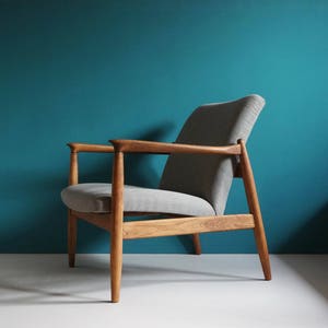 May include: A mid-century modern armchair with a light gray fabric upholstery and a wooden frame. The chair has a high back and angled arms.