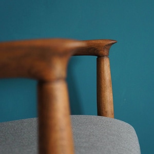 May include: Close-up of a wooden chair with a gray fabric seat. The chair has a curved back and a simple design.