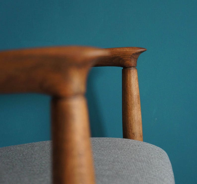 May include: Close-up of a wooden chair with a gray fabric seat. The chair has a curved back and a simple design.