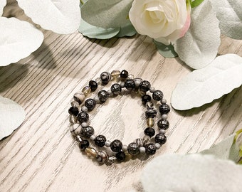 May include: A black and white beaded bracelet with a mix of round and faceted beads. The bracelet is layered with a second strand of smaller beads.