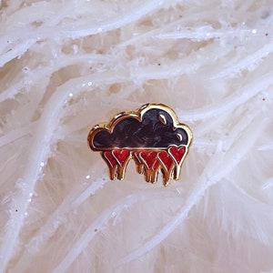 May include: Gold-tone pin with a black cloud shape and red hearts raining from it.