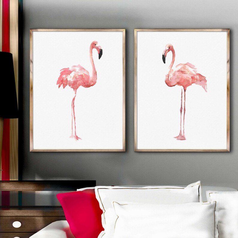 May include: Two framed watercolor paintings of pink flamingos on a white background. The flamingos are standing on one leg with their necks curved.
