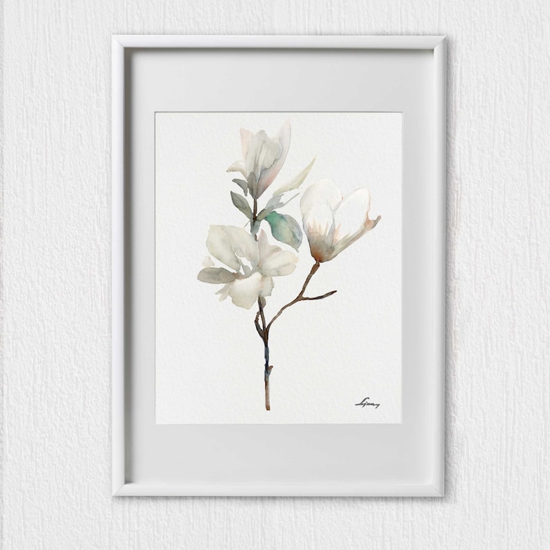 Pode incluir: Uma pintura em aquarela de um ramo de flor de magn&oacute;lia branca com folhas verdes. A pintura est&aacute; emoldurada em uma moldura branca.