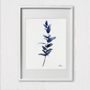 Pu&ograve; includere: Un dipinto ad acquerello incorniciato di un ramo di eucalipto blu su sfondo bianco. Il dipinto &egrave; firmato "Spring" in basso a destra.