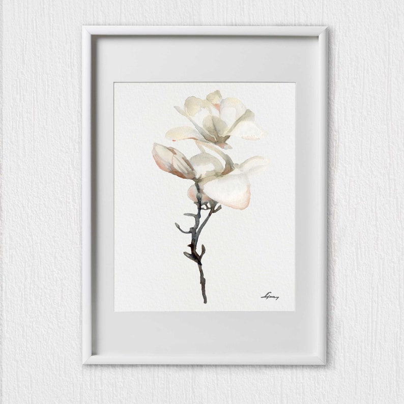 Pode incluir: Uma pintura em aquarela de uma flor de magn&oacute;lia branca com um caule e folhas delicados. A pintura est&aacute; emoldurada em uma moldura branca.