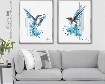 May include: Two watercolor paintings of hummingbirds in flight. The hummingbirds are painted in shades of blue and green, with splashes of white and pink. The paintings are set against a white background with a subtle gray frame.