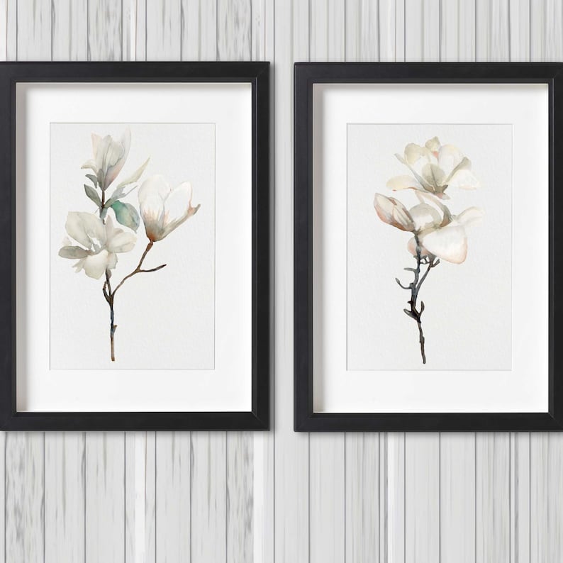 Pode incluir: Duas impress&otilde;es emolduradas em preto com um passe-partout branco, cada uma com uma pintura em aquarela de uma flor de magn&oacute;lia branca sobre um fundo branco.