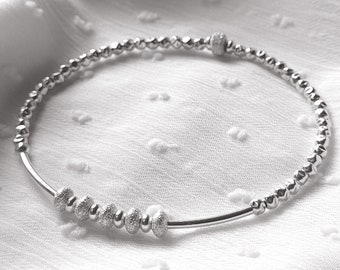 Könnte beinhalten: Ein silbernes Armband mit Perlen und einer Reihe größerer, strukturierter Perlen in der Mitte.