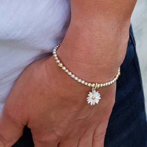 May include: A silver and gold beaded bracelet with a small silver daisy charm.