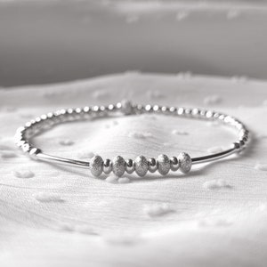 May include: A silver bracelet with a row of textured beads in the center.