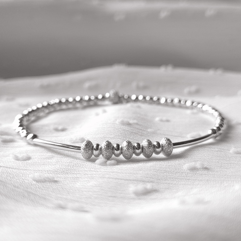 May include: A silver bracelet with a row of textured beads in the center.