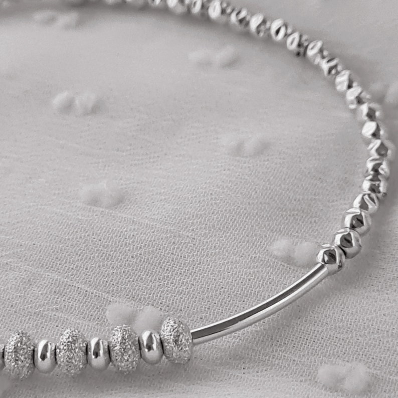 May include: A silver bracelet with small, textured beads. The bracelet is made of a thin, silver band with a row of beads that are slightly larger and textured.