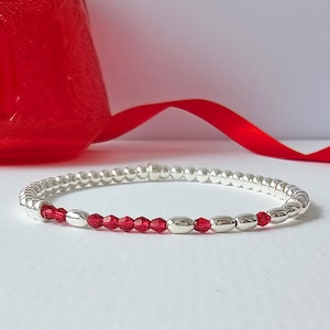 Peut inclure: Un bracelet argenté avec une rangée de perles de cristal rouge.