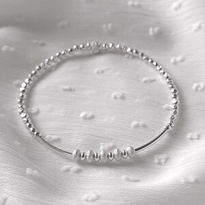 May include: A silver beaded bracelet with a row of larger, textured beads in the center.