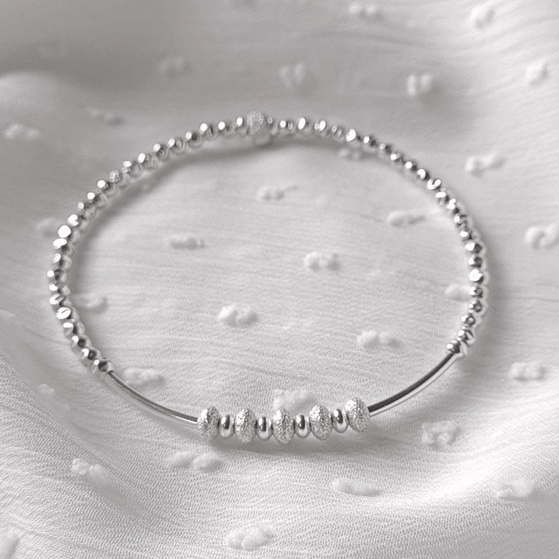 May include: A silver beaded bracelet with a row of larger, textured beads in the center.