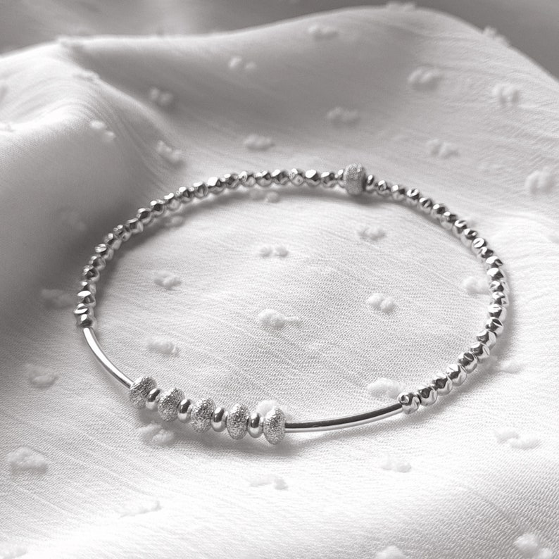 May include: A silver beaded bracelet with a row of larger, textured beads in the center.