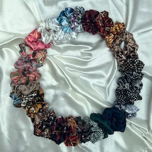 Könnte beinhalten: Eine Sammlung von bunten und gemusterten Haargummis aus verschiedenen Stoffen, darunter Blumen, Paisley und Punkte.