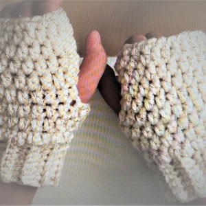 Könnte beinhalten: Ein Paar fingerlose Handschuhe aus weißem Garn mit einem dezenten Schimmer. Die Handschuhe sind gehäkelt und haben ein strukturiertes Muster.