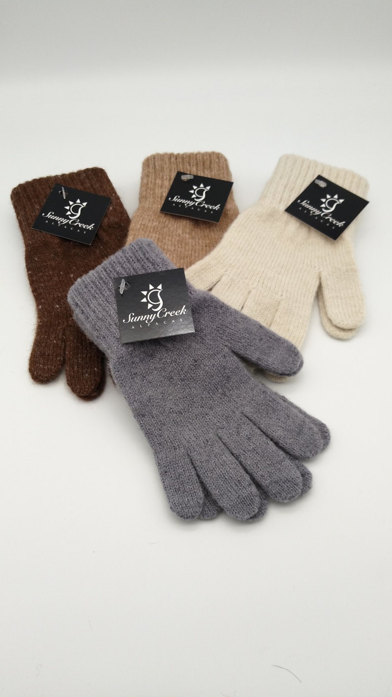 May include: Three pairs of alpaca gloves in brown, beige, and gray. Each pair has a black tag with the words "Sunny Creek Alpaca" and a sun graphic.