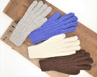 May include: Four pairs of knitted gloves in different colors: gray, blue, white, and brown. The gloves have a cable knit pattern and are displayed on a wooden surface.