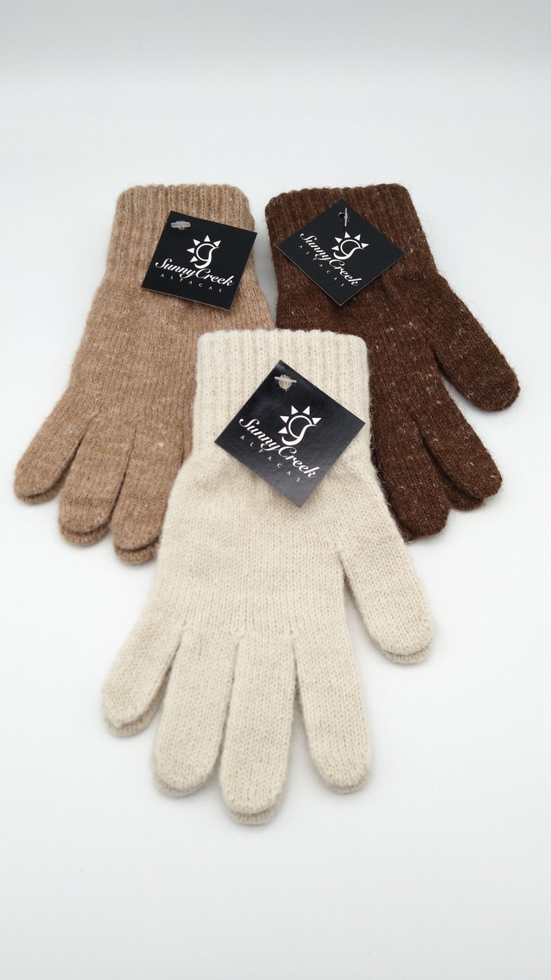 May include: Three pairs of alpaca gloves in brown, beige, and white. Each pair has a black tag with the words "Sunny Creek Alpacas" and a sun graphic.
