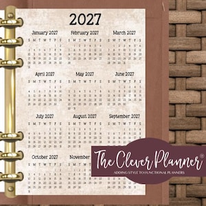 May include: A 2027 yearly calendar page with a textured beige background, featuring twelve monthly grids. The calendar is held by a gold-colored metal ring binder mechanism. A dark purple rectangular label displays the text The Clever Planner.