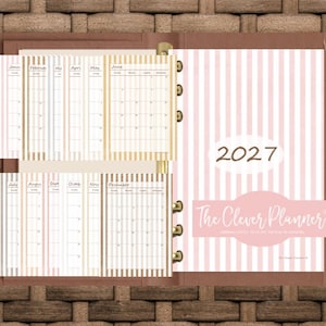 May include: A 2027 planner titled The Clever Planner with a pink and white striped cover. The interior features monthly calendar pages for January through December, organized with vertical stripes and a ring-bound metal spine mechanism.