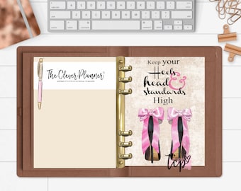 May include: A brown leather planner with gold rings. The front cover has a beige background with the text "The Clever Planner" and a pink pen. The back cover has a beige background with the text "Keep your heels & head standards High" and a pink bow on top of a black high heel shoe.