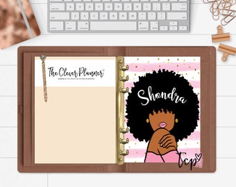 May include: A brown leather planner with gold rings. The front cover has a pink and white striped background with gold glitter. The cover also features a black and white illustration of a woman with an afro and the text "Shondra" and "tep".