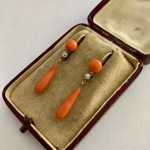 Pu&ograve; includere: Un paio di orecchini pendenti vintage in corallo e diamanti. Gli orecchini sono in oro e presentano una pietra di corallo a forma di lacrima con un piccolo accento di diamante.