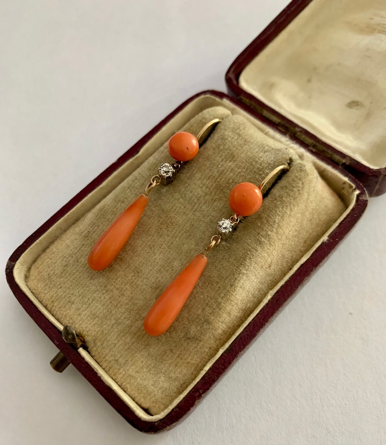 Pu&ograve; includere: Un paio di orecchini pendenti vintage in corallo e diamanti. Gli orecchini sono in oro e presentano una pietra di corallo a forma di lacrima con un piccolo accento di diamante.