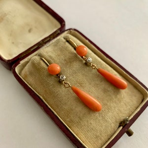 Pu&ograve; includere: Un paio di orecchini d'oro con dettagli in corallo e diamanti. Gli orecchini sono in una piccola scatola di velluto rosso.